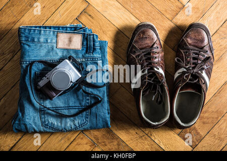 A pair of fretted blue jeans, brown shoes, and a camera lie by on the floor. Stock Photo