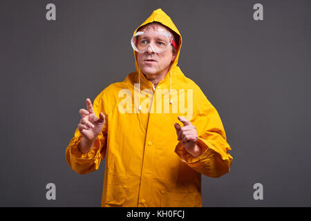 A middle aged man standing and thinking in a yellow raincoat Stock Photo