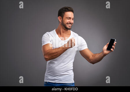 A handsome young man holding and showing his phone and celebrating Stock Photo