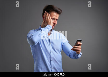 A handsome young man looking at a smartphone and feeling frustrated and grabbing his head Stock Photo