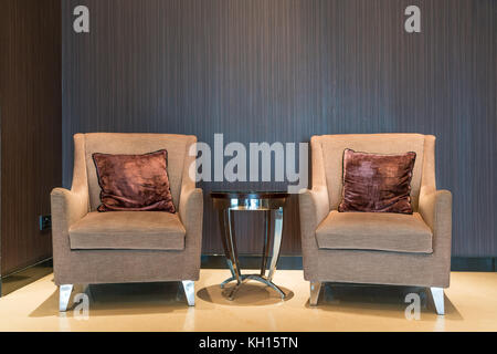 Leather armchair and coffee table in lobby at hotel. Interior design of classic leather chair in dim room. Stock Photo