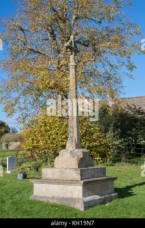 Stone cross gravestone in St Mary's Church churchyard in autumn. Swinbrook, Oxfordshire, England Stock Photo