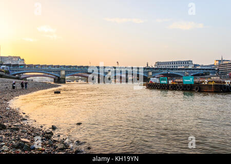 Sunset behind Blackfriars Bridge and railway station seen from the Thames foreshore at Bankside, at low tide on an autumn evening Stock Photo