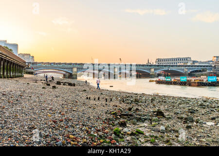 Sunset behind Blackfriars Bridge and railway station seen from the Thames foreshore at Bankside, at low tide on an autumn evening Stock Photo