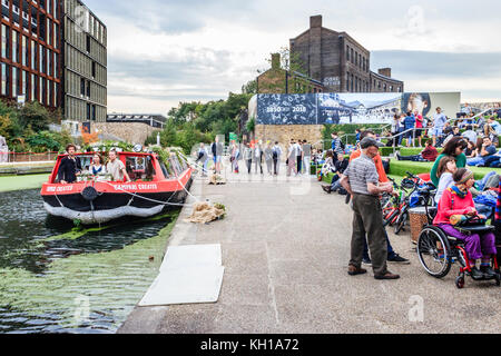 People socialising on the artificial-grassed steps at Granary Square, King's Cross, London, UK, by the Regent's Canal, 2017 Stock Photo