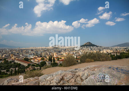 The City of Athens spreads out below Mars Hill where rocks in the foreground have been adorned by grafitti.  Light white clouds float in the azure blu