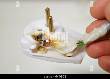 Close-up of a hand holding a burnt plug with plastic that is burned in a fire as a result of lightning damage or a surge in electrical voltage Stock Photo