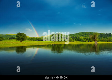 Rainbow over a lake, reflected in the water. Stock Photo