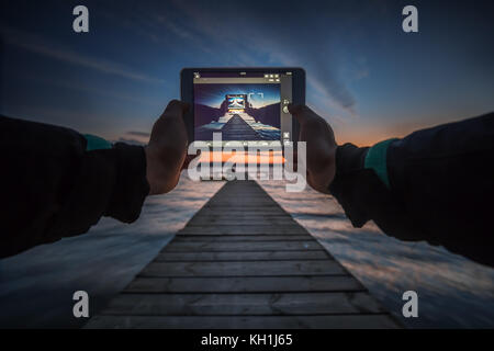 Close-up shot of working tablet on sunset and sea background Stock Photo