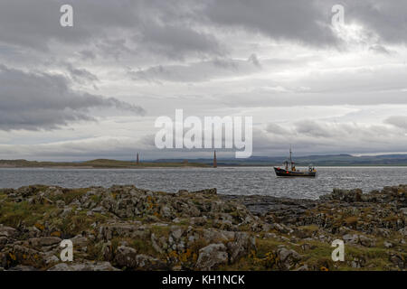 Shell fishing vessel Britannia II operating off Guile Island at Holy Island with the Old Law navigation aids in the background Stock Photo