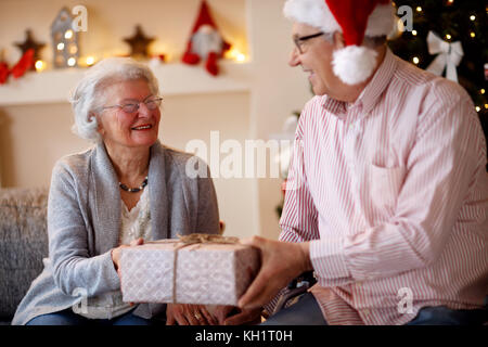 Happy beautiful elderly couple celebrating Christmas at home with presents Stock Photo