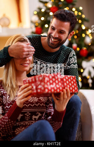 smiling young man covering woman's eyes with hands and giving gift box Stock Photo