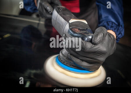 Close-up of a male mechanic with a blue prism and protective gloves will flicker the black metal bumper machine from small scratches after painting Stock Photo