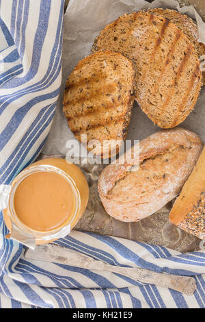 Whole wheat bread buns and grilled  bread slices, with opened jar of peanut butter and knife. Stock Photo