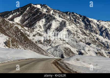 Scenic winter view with the winding asphalt road on a background of mountains covered with snow Stock Photo