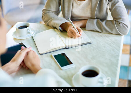 Closeup of two unrecognizable businesswomen working in cafe writing notes in planner and drinking coffee Stock Photo