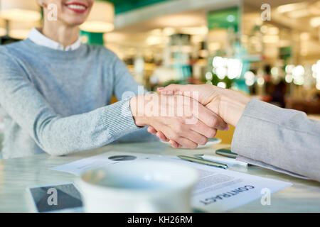 Closeup image of two businesswomen shaking hands over contract celebrating successful business deal during meeting in cafe Stock Photo