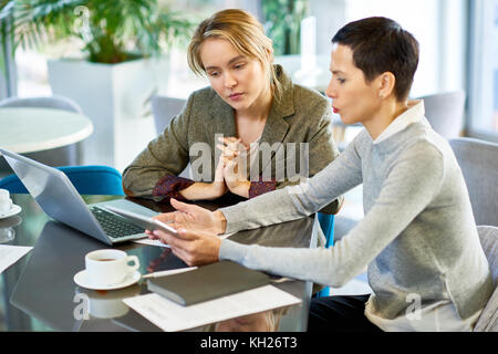 Portrait of two businesswomen discussing work and using laptop during business meeting in modern office Stock Photo