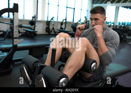 Portrait of handsome muscular man doing crunches on stand during work out in modern gym Stock Photo