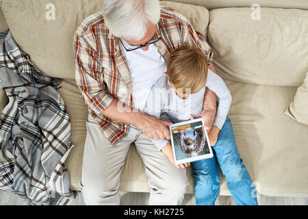High angle view of grandfather and grandson using digital tablet looking at photos together at home Stock Photo
