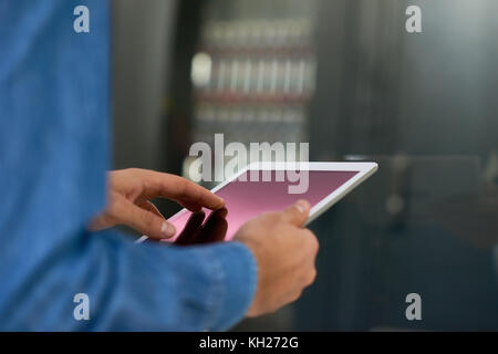 Closeup of systems administrator using digital tablet against bacground of server cabinet, copy space Stock Photo