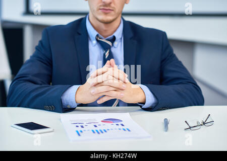 Mid-section portrait of unrecognizable business analyst sitting at desk in office with hands clasped looking at data graph Stock Photo