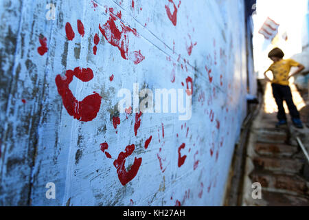 Young boy in the narrow street looking at hand print on the wall of a blue house, Jodhpur, Rajasthan, India. Stock Photo