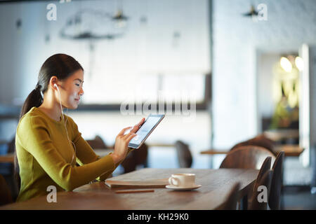 Modern teenager with tablet watching online video by cup of coffe in cafe Stock Photo