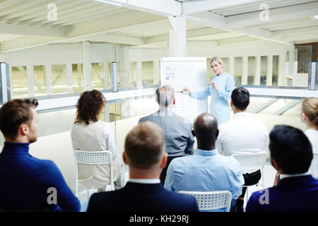 Group of students listening to experienced coach explaining chart and diagram on whiteboard Stock Photo