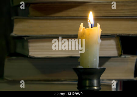 Burning candle against the background of a stack of old books Stock Photo