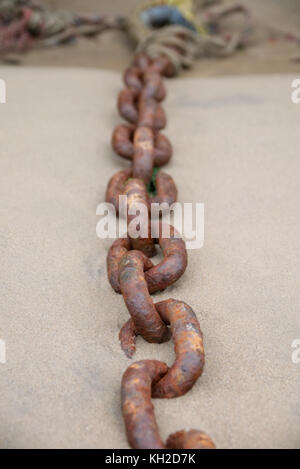 Rusty old boat chain on a sandy beach with a shallow depth of field Stock Photo
