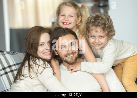 Portrait of happy cheerful young family bonding together, smiling kids embracing parents indoors, son and daughter with mother hugging dad posing look Stock Photo