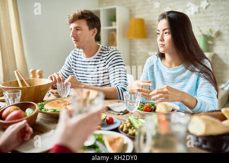 Portrait of two modern young people sitting at big table with food having dinner with friends and listening to conversation celebrating holiday with f Stock Photo