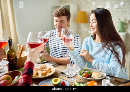 Group portrait of friends enjoying dinner together sitting at big table with delicious food , focus on young man and pretty Asian woman smiling happil Stock Photo