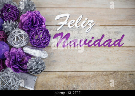 Group of purple and silver Christmas decoration on a wooden background with text in Spanish 'Feliz Navidad'. Stock Photo