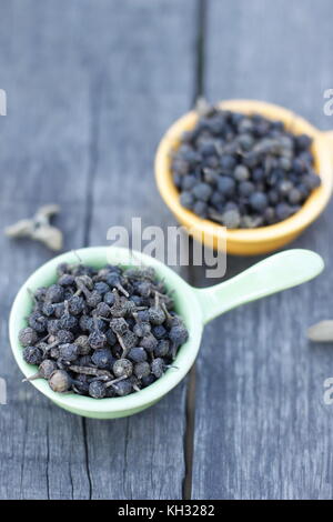 Cubeb pepper in green and yellow bowls over wooden board Stock Photo