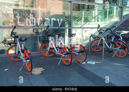 Mobikes that can be hired for use by a mobile phone app have a GPS tracker fitted here parked outside the Central Library on a littered pavement Stock Photo