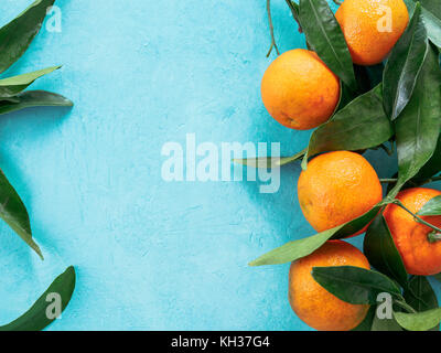 Tangerines, oranges, mandarins, clementines, citrus fruits with leaves on blue concrete background. Top view or flat-lay. Copy space. Stock Photo