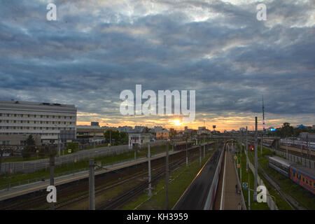 Cityscape with many railway tracks and movement of commuter passenger electric train on them. Movement of the clouds with sunset at the background. Stock Photo