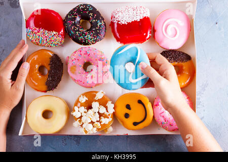 Hands holding box and choosing sweet doughnuts on gray stone background Stock Photo