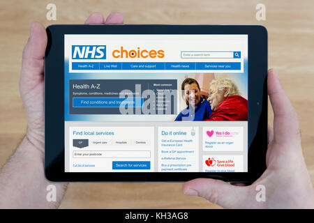 A man looks at the NHS Choices website on his iPad tablet device, shot against a wooden table top background (Editorial use only) Stock Photo