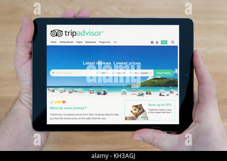 A man looks at the Trip Advisor website on his iPad tablet device, shot against a wooden table top background (Editorial use only) Stock Photo
