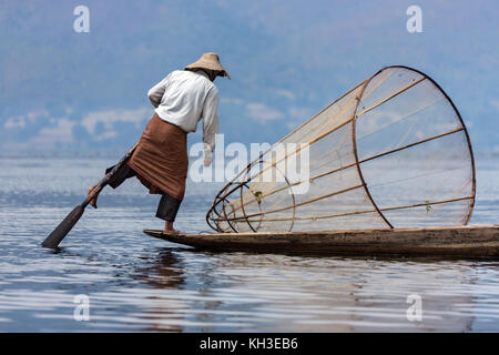 A leg rowing fisherman on Inle Lake in Shan State in Myanmar (Burma).This unique style of rowing evolved because the shallow lake bottom is covered by Stock Photo