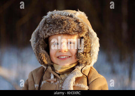 A portrait of smiling, lovely  little child boy wearing sheepskin cap and hood. Close up of young kid, looking at camera, happy Stock Photo