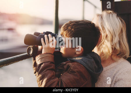 Little caucasian boy watching, gazing, looking, searching for by binoculars with mother in sunset Stock Photo