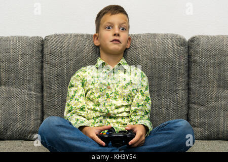 Boy playing video games with joystic sitting on sofa Stock Photo