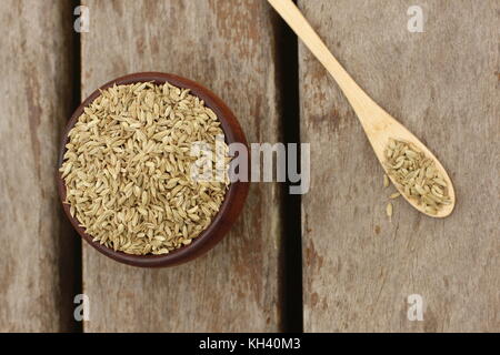 Wooden bowl filled with fennel seeds and a wooden spoon with fennel seeds over a wooden deck Stock Photo