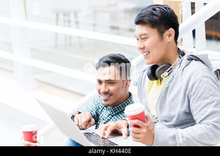Two young Asian men using a laptop while relaxing during break Stock Photo