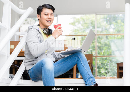 Happy young Asian employee using a laptop in a modern office Stock Photo