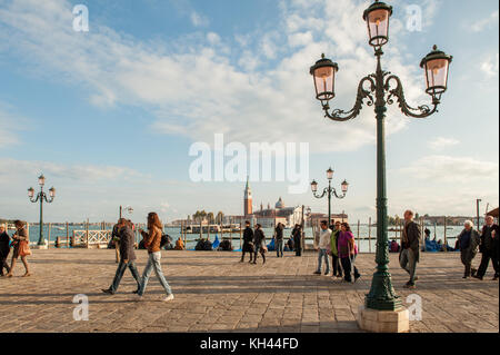 Tourists enjoying a walk at the waterfront Riva degli Schiavoni in San Marco. Venice is a major tourist destination in Italy. Stock Photo